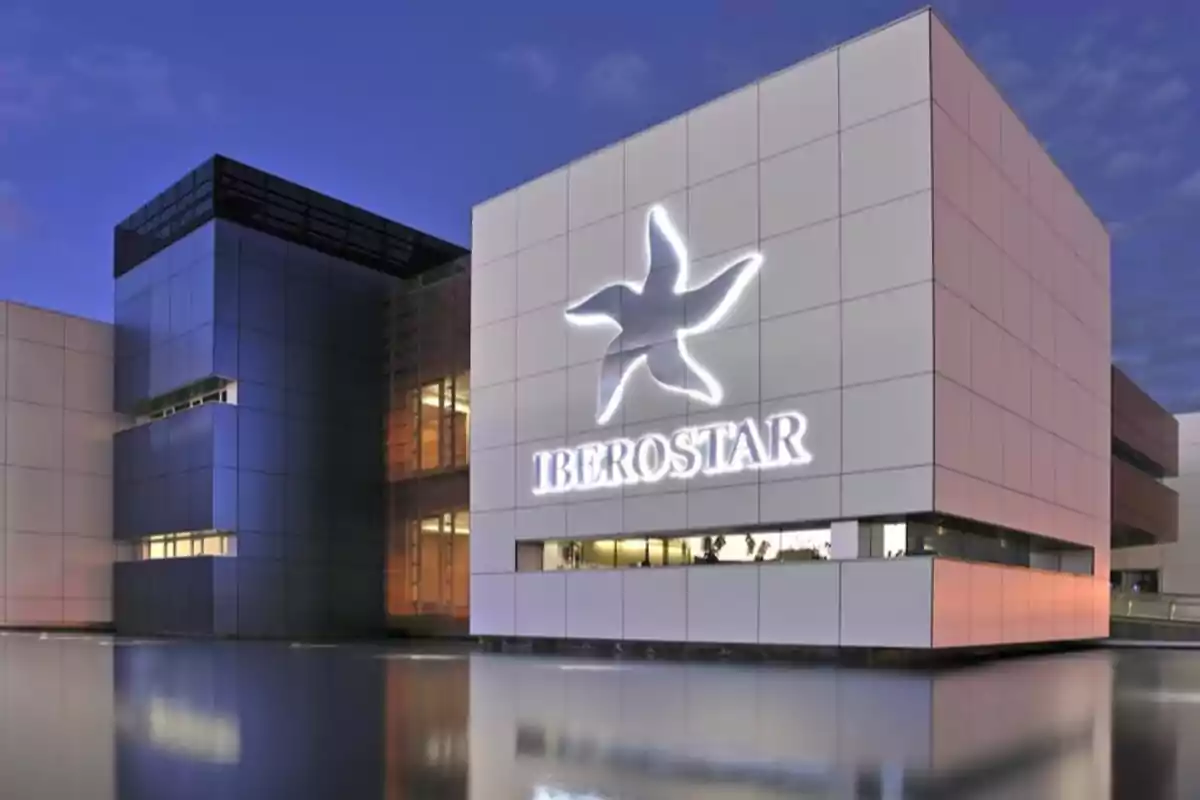 Edificio moderno con el logo iluminado de Iberostar reflejado en el agua al atardecer Edificio moderno con el logo iluminado de Iberostar reflejado en el agua al atardecer