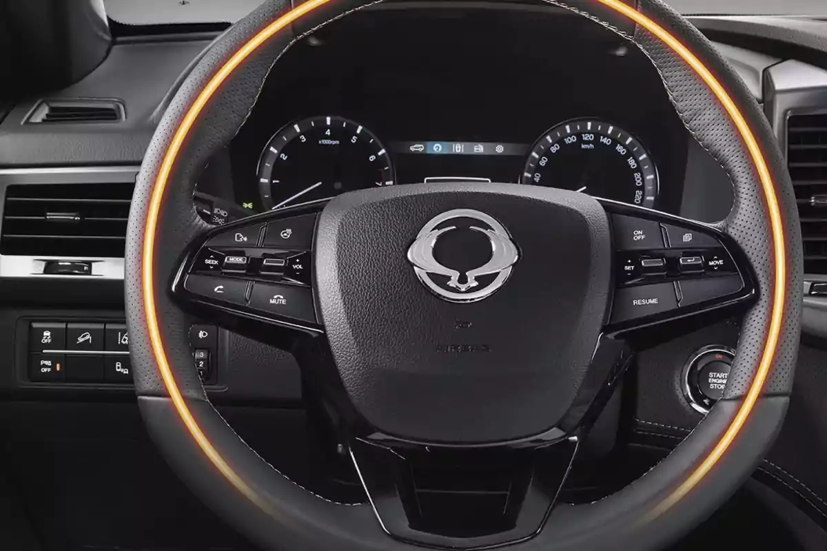 Volante de automóvil con detalles iluminados en color naranja y múltiples controles integrados, tablero digital al fondo y botón de encendido a la derecha Volante de automóvil con detalles iluminados en color naranja y múltiples controles integrados, tablero digital al fondo y botón de encendido a la derecha