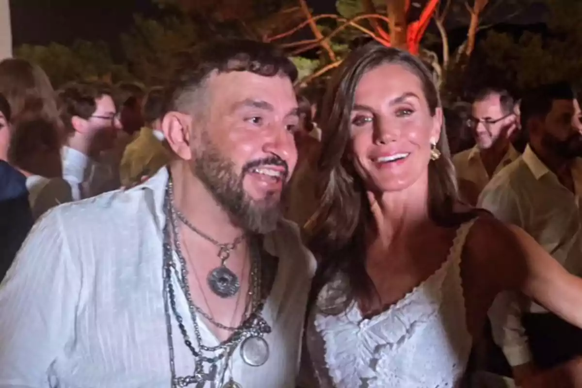 Dos personas sonríen y posan juntas en una fiesta al aire libre durante la noche rodeadas de más asistentes Dos personas sonríen y posan juntas en una fiesta al aire libre durante la noche rodeadas de más asistentes
