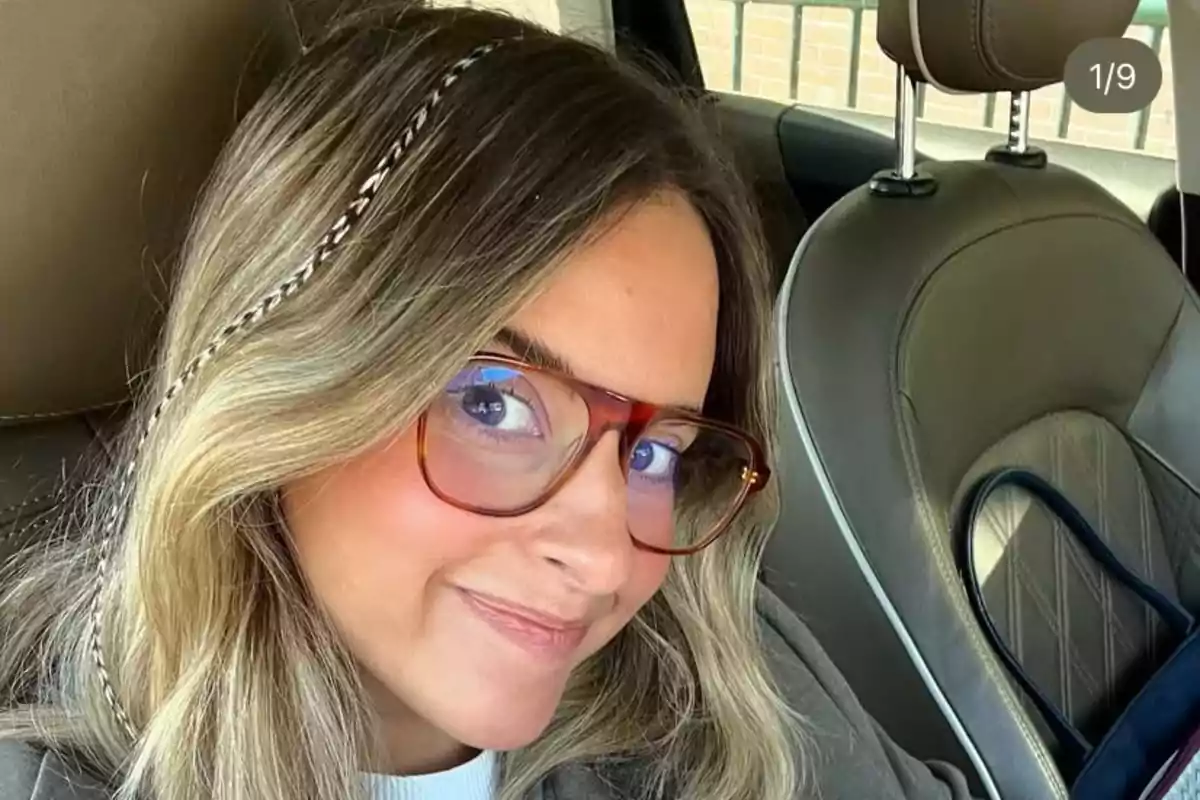 Mujer joven con gafas grandes y cabello rubio con una trenza decorativa sentada en el asiento del conductor de un auto