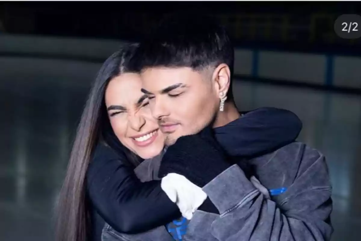 Una pareja joven se abraza con expresiones de felicidad y cariño en un ambiente interior iluminado suavemente