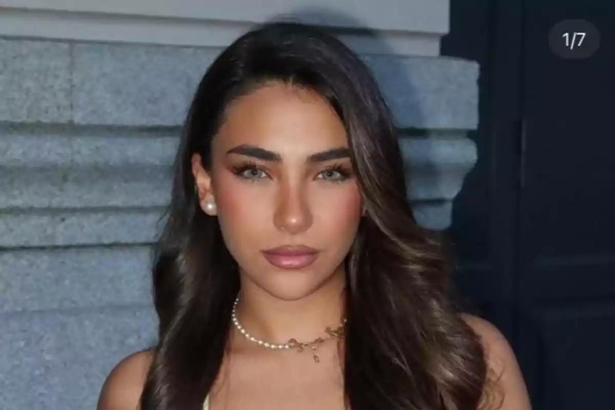 Mujer joven de cabello largo y oscuro con maquillaje natural y collar de perlas posando frente a una pared de piedra. Mujer joven de cabello largo y oscuro con maquillaje natural y collar de perlas posando frente a una pared de piedra.