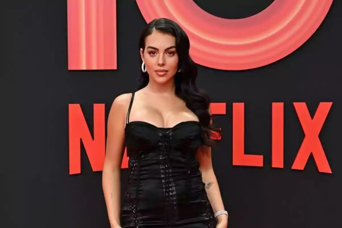 Mujer con vestido negro posando frente a un fondo con el logo de Netflix en letras rojas
