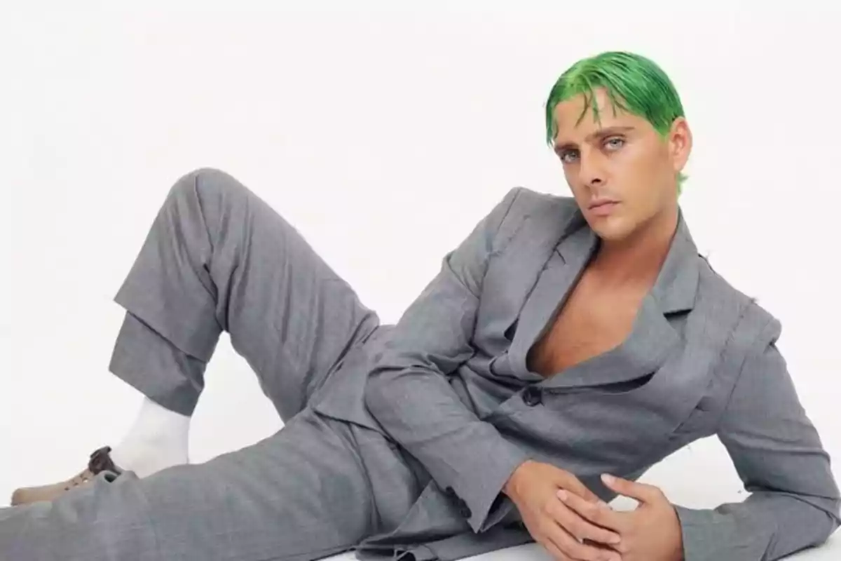 Persona con cabello verde y traje gris posando recostada sobre el suelo en un fondo blanco Persona con cabello verde y traje gris posando recostada sobre el suelo en un fondo blanco