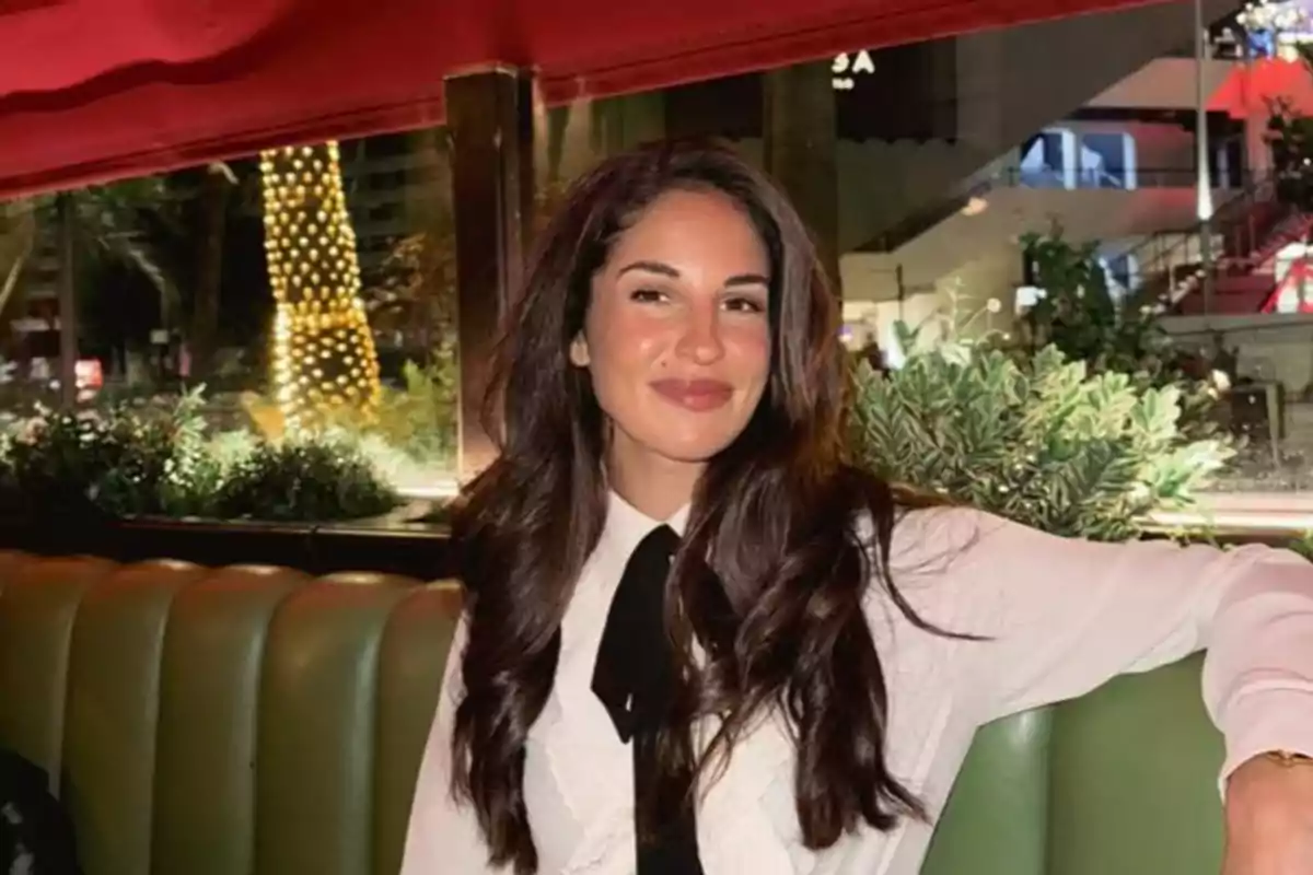 Mujer joven con cabello largo y oscuro sentada en un restaurante elegante con luces y plantas al fondo Mujer joven con cabello largo y oscuro sentada en un restaurante elegante con luces y plantas al fondo