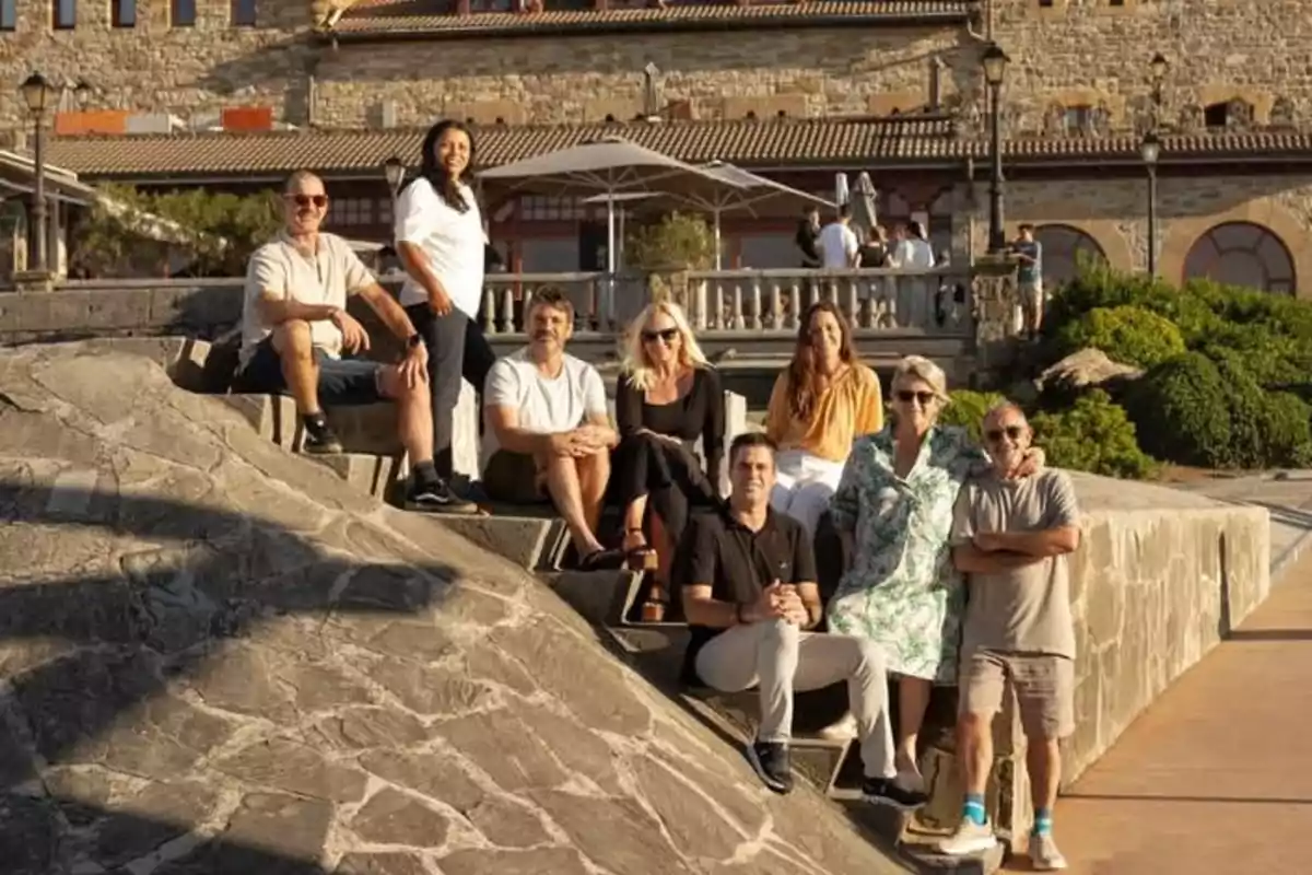 Un grupo de personas posa sentado y de pie en unas escaleras de piedra al aire libre con un edificio antiguo de fondo en un día soleado