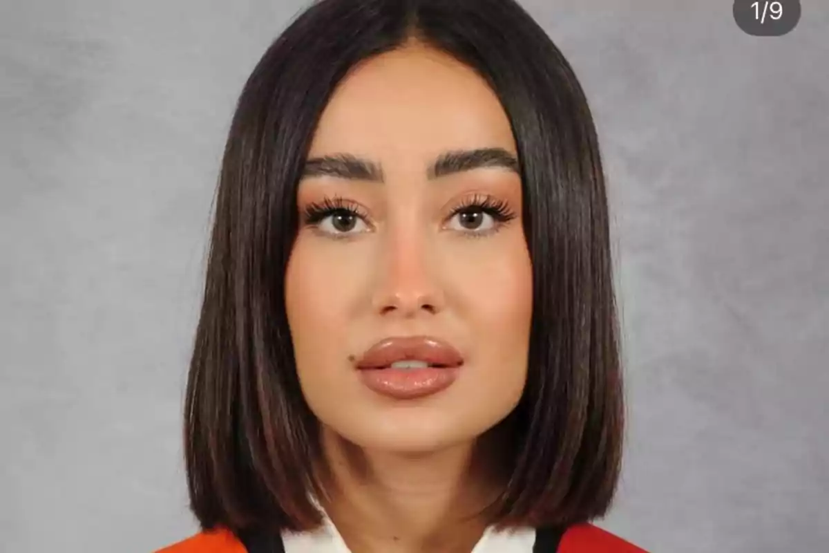 Retrato de una mujer joven con cabello lacio y corto, piel clara y labios maquillados, usando una prenda roja y fondo gris.