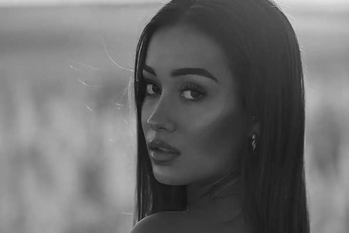 Mujer joven de cabello largo mirando sobre su hombro en una fotografía en blanco y negro