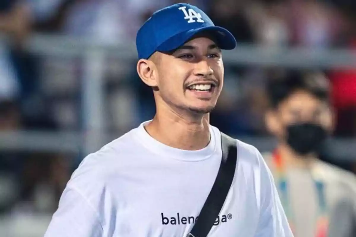 Hombre joven sonriendo con gorra azul y camiseta blanca en un evento deportivo Hombre joven sonriendo con gorra azul y camiseta blanca en un evento deportivo