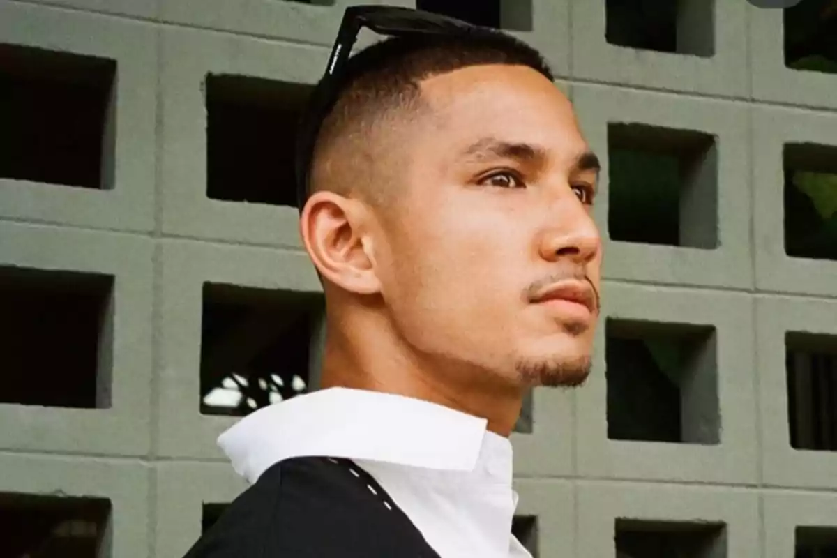 Joven con barba corta y gafas en la cabeza mirando hacia la derecha frente a una pared de bloques grises
