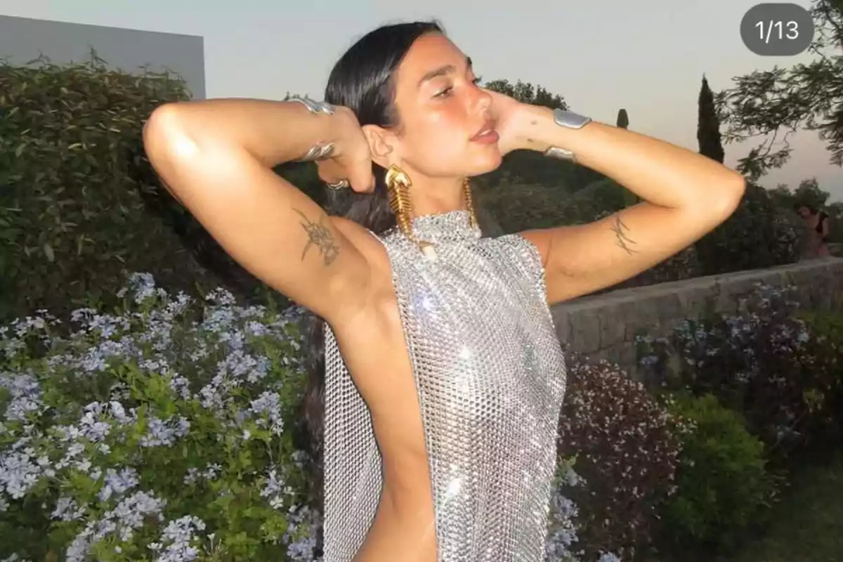 Mujer con vestido plateado brillante y aretes dorados posando al aire libre con flores y vegetación de fondo Mujer con vestido plateado brillante y aretes dorados posando al aire libre con flores y vegetación de fondo