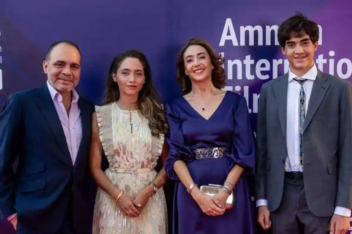 Cuatro personas elegantemente vestidas posan sonrientes frente a un fondo púrpura en un evento formal
