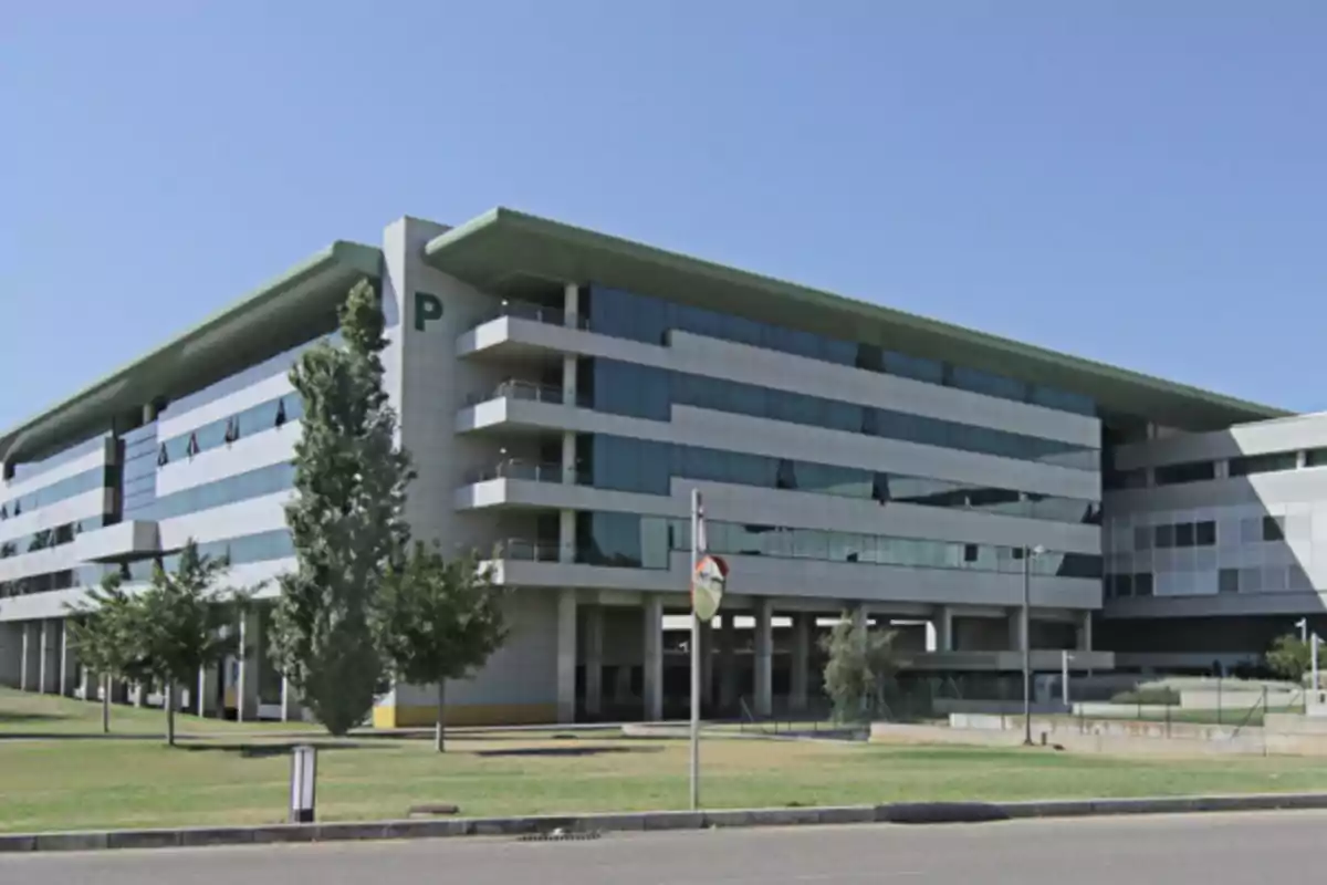 Edificio moderno de varios pisos con fachada de vidrio y áreas verdes al frente en un día soleado