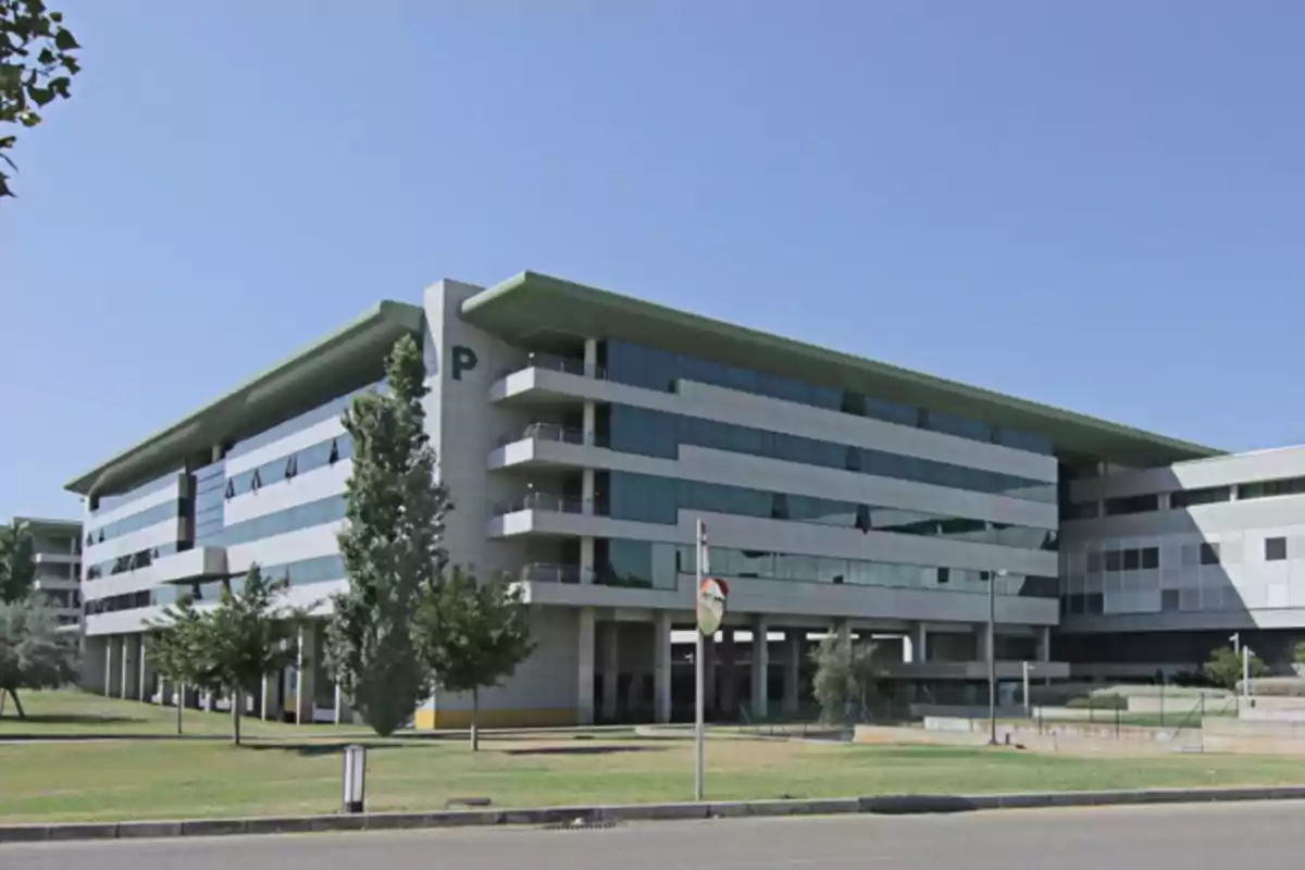 Edificio moderno de oficinas con fachada de vidrio y áreas verdes al frente en un día soleado Edificio moderno de oficinas con fachada de vidrio y áreas verdes al frente en un día soleado
