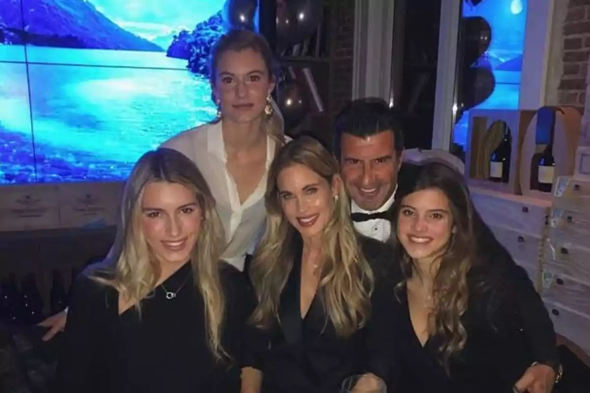 Cinco personas posan sonrientes en una fiesta elegante con un fondo de pantalla que muestra un paisaje de lago y montañas