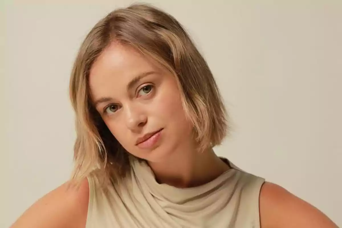 Mujer joven de cabello rubio corto y lacio con expresión serena y fondo beige