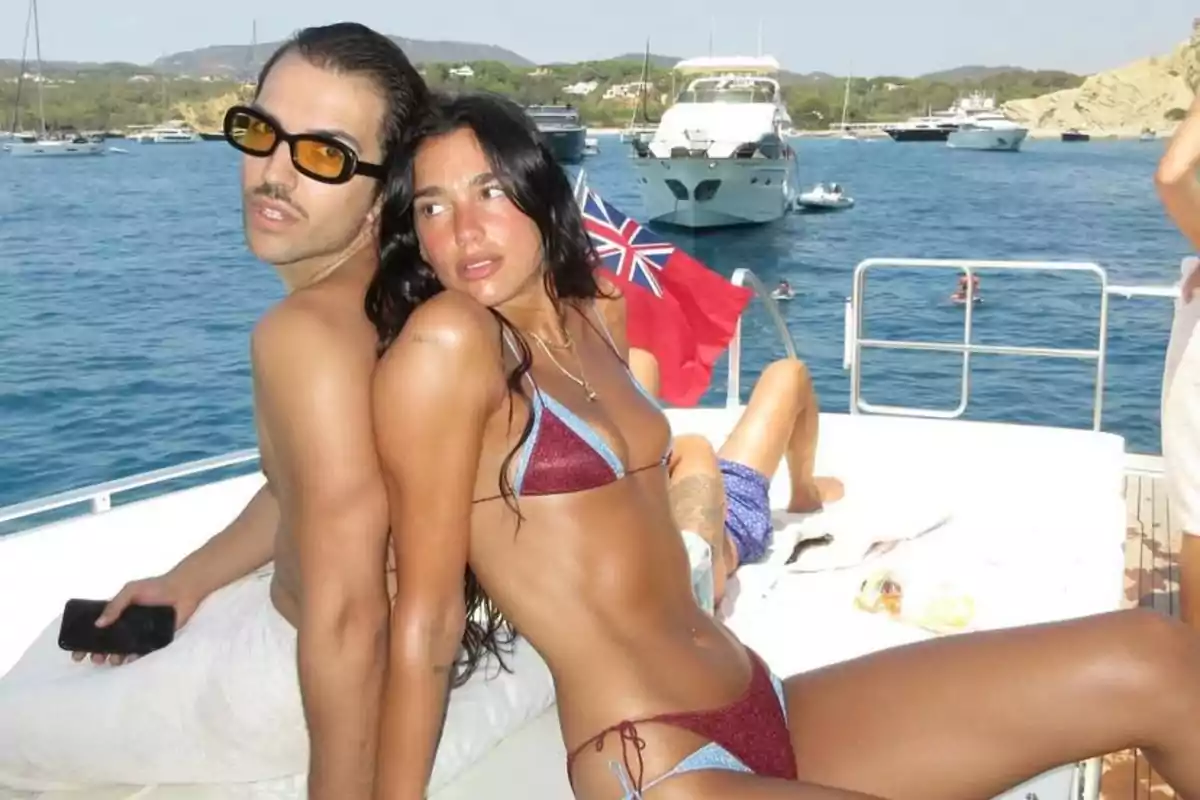 Dos personas en traje de baño posan sentadas de espaldas en la cubierta de un yate con el mar y varios barcos al fondo en un día soleado Dos personas en traje de baño posan sentadas de espaldas en la cubierta de un yate con el mar y varios barcos al fondo en un día soleado