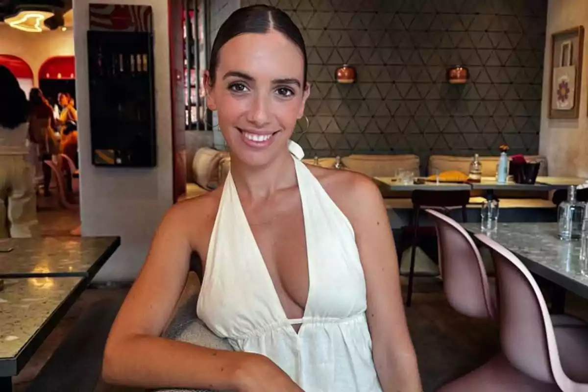 Mujer joven con vestido blanco sonríe sentada en una mesa de un restaurante moderno