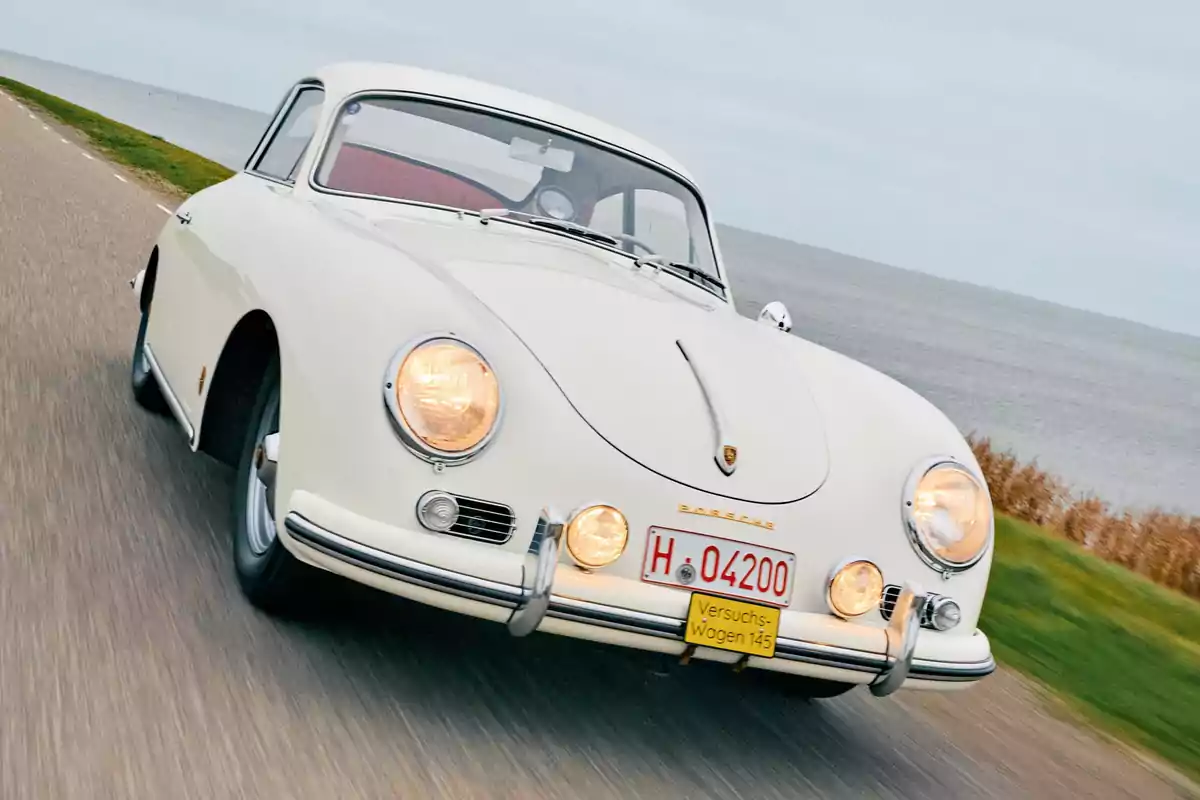 Auto clásico Porsche blanco conduciendo por una carretera junto al mar Auto clásico Porsche blanco conduciendo por una carretera junto al mar