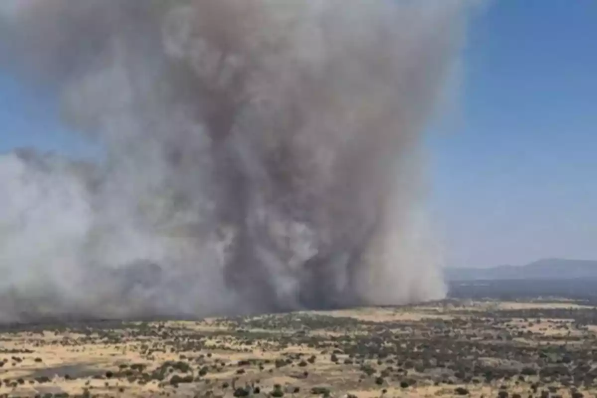 Gran columna de humo elevándose sobre un paisaje árido debido a un incendio forestal Gran columna de humo elevándose sobre un paisaje árido debido a un incendio forestal