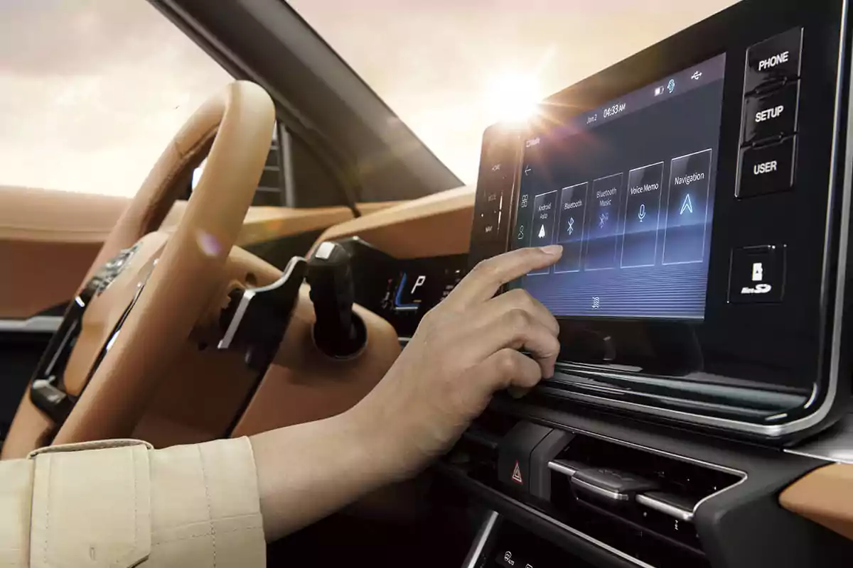 Persona usando la pantalla táctil del sistema de entretenimiento de un automóvil moderno con interior en color beige y volante visible Persona usando la pantalla táctil del sistema de entretenimiento de un automóvil moderno con interior en color beige y volante visible