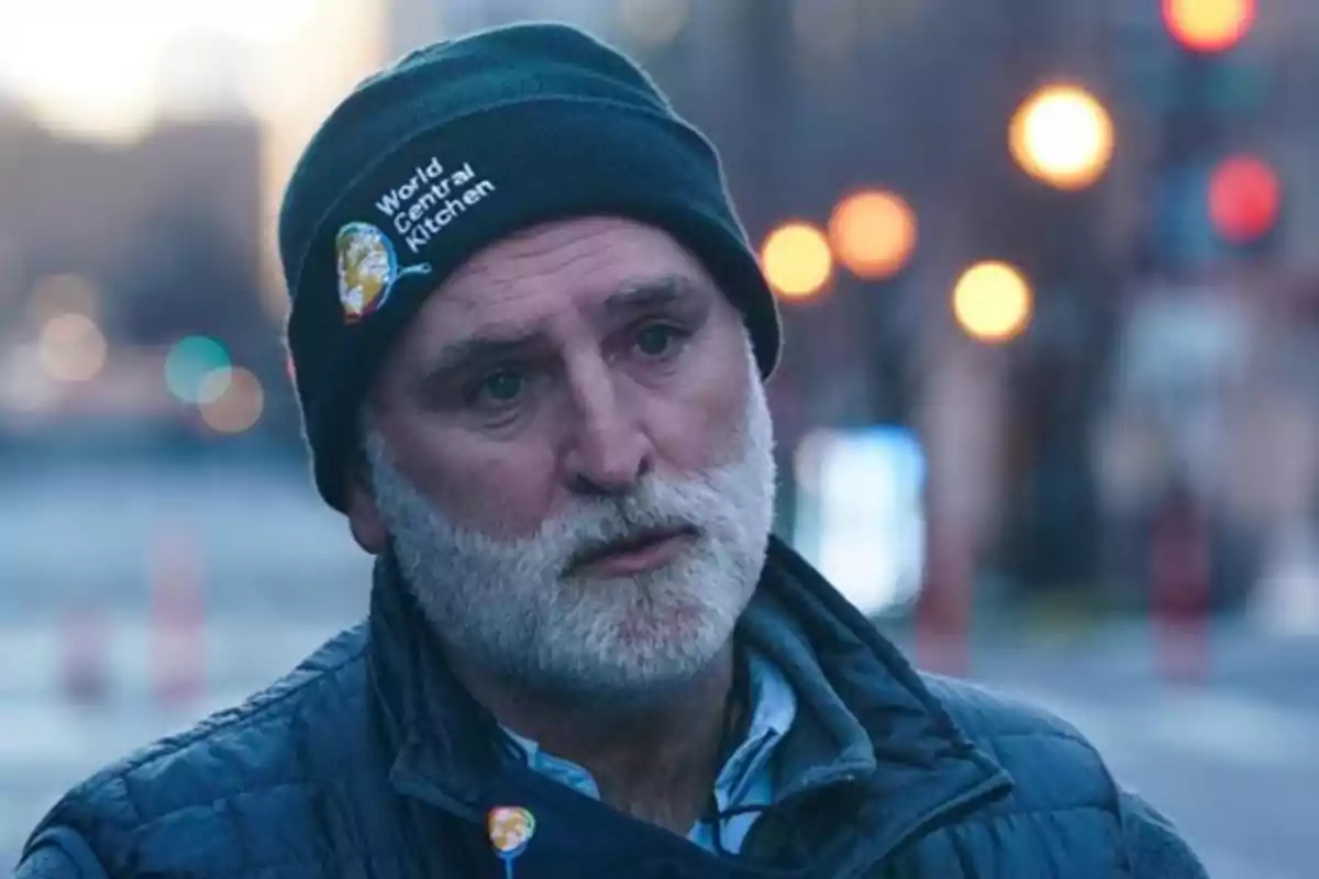 Hombre de barba canosa con gorro negro de World Central Kitchen y chaqueta azul en una calle desenfocada al atardecer Hombre de barba canosa con gorro negro de World Central Kitchen y chaqueta azul en una calle desenfocada al atardecer