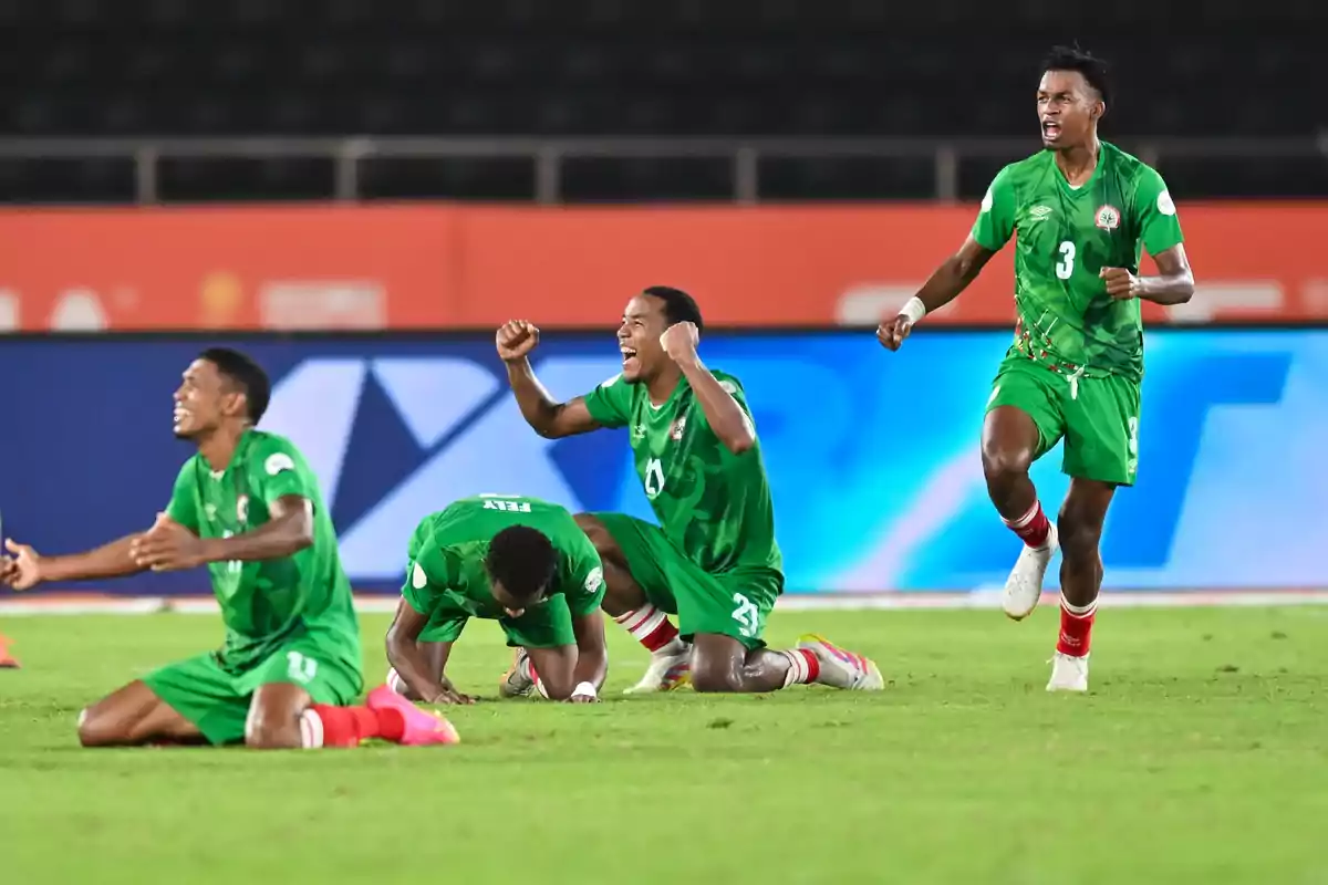 Cuatro futbolistas con uniforme verde celebran emocionados en el campo de fútbol tras un partido