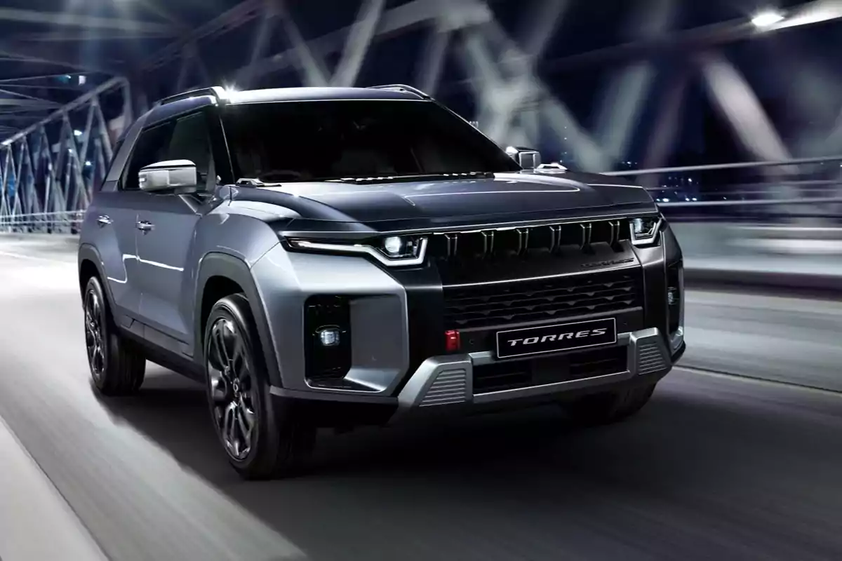 SUV gris de aspecto moderno circulando por un puente iluminado durante la noche SUV gris de aspecto moderno circulando por un puente iluminado durante la noche