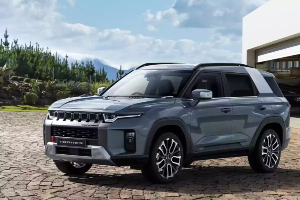 SUV gris estacionada sobre un camino de adoquines frente a una casa moderna con vegetación y montañas al fondo SUV gris estacionada sobre un camino de adoquines frente a una casa moderna con vegetación y montañas al fondo