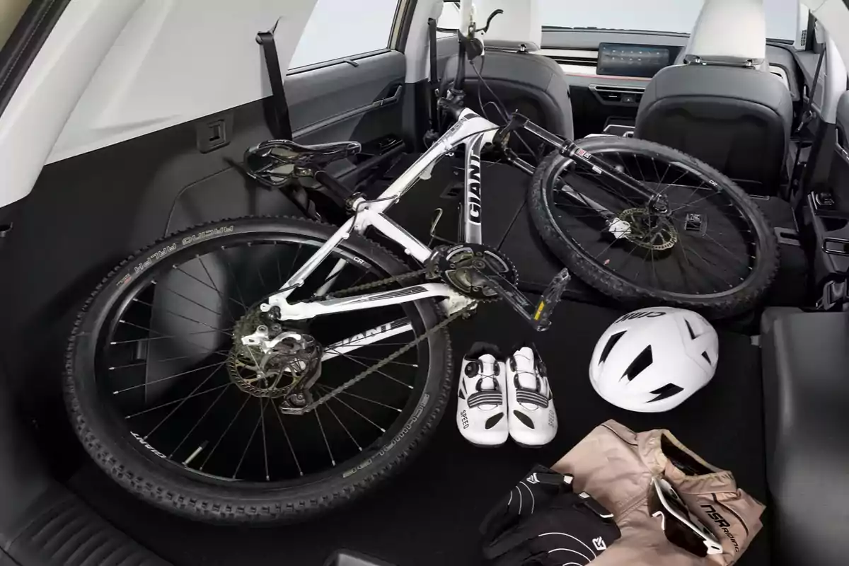 Una bicicleta de montaña desmontada junto a un casco, unos guantes, unos zapatos y una chaqueta dentro de la cajuela de un auto Una bicicleta de montaña desmontada junto a un casco, unos guantes, unos zapatos y una chaqueta dentro de la cajuela de un auto