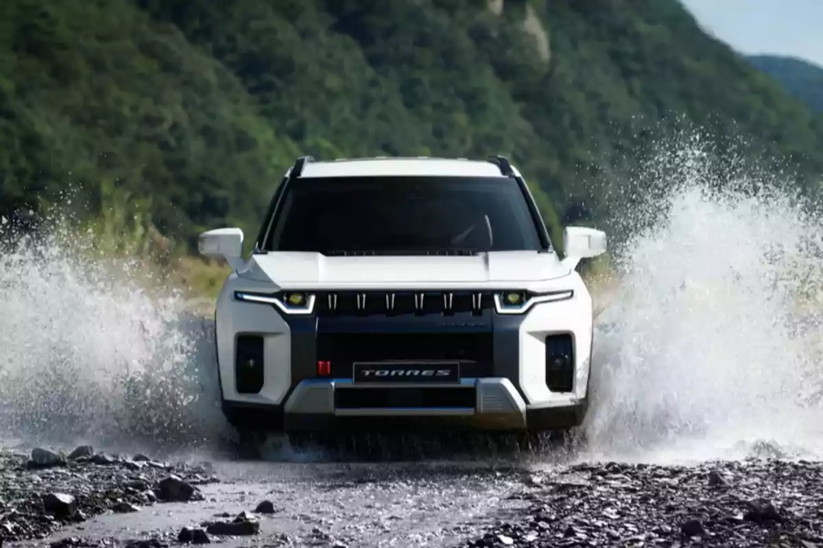 SUV blanca cruzando un arroyo con agua salpicando a los lados y vegetación al fondo