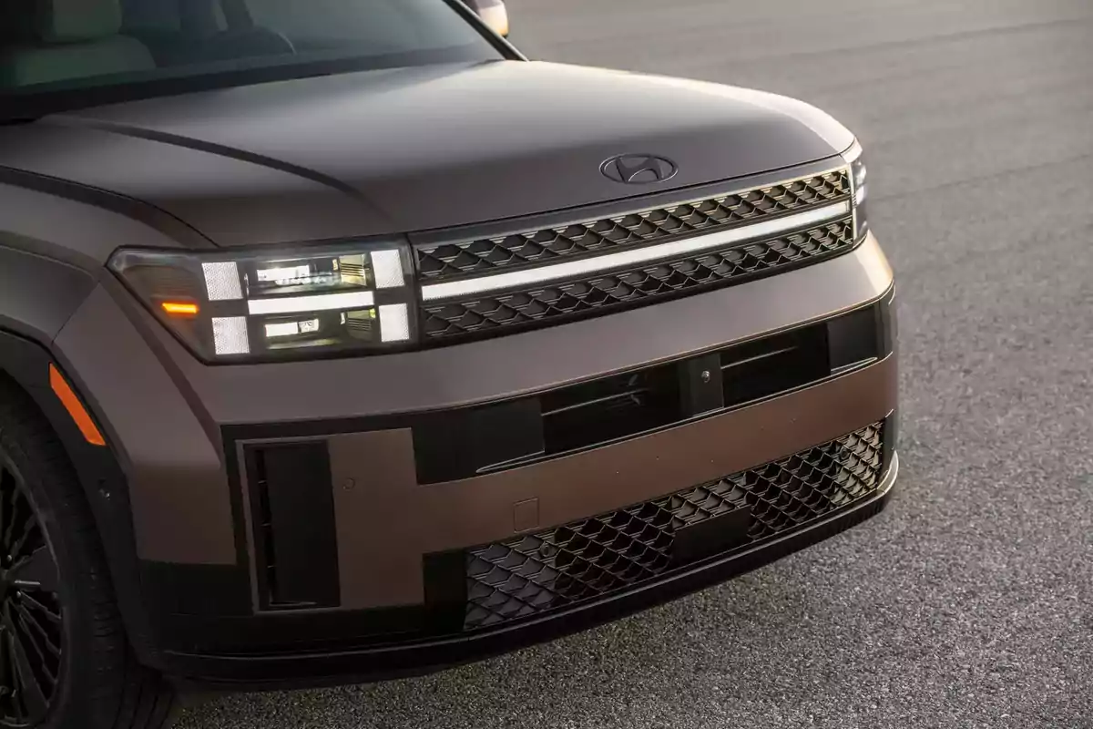 Frente de un vehículo SUV color marrón con faros LED cuadrados y parrilla de diseño geométrico estacionado sobre asfalto Frente de un vehículo SUV color marrón con faros LED cuadrados y parrilla de diseño geométrico estacionado sobre asfalto