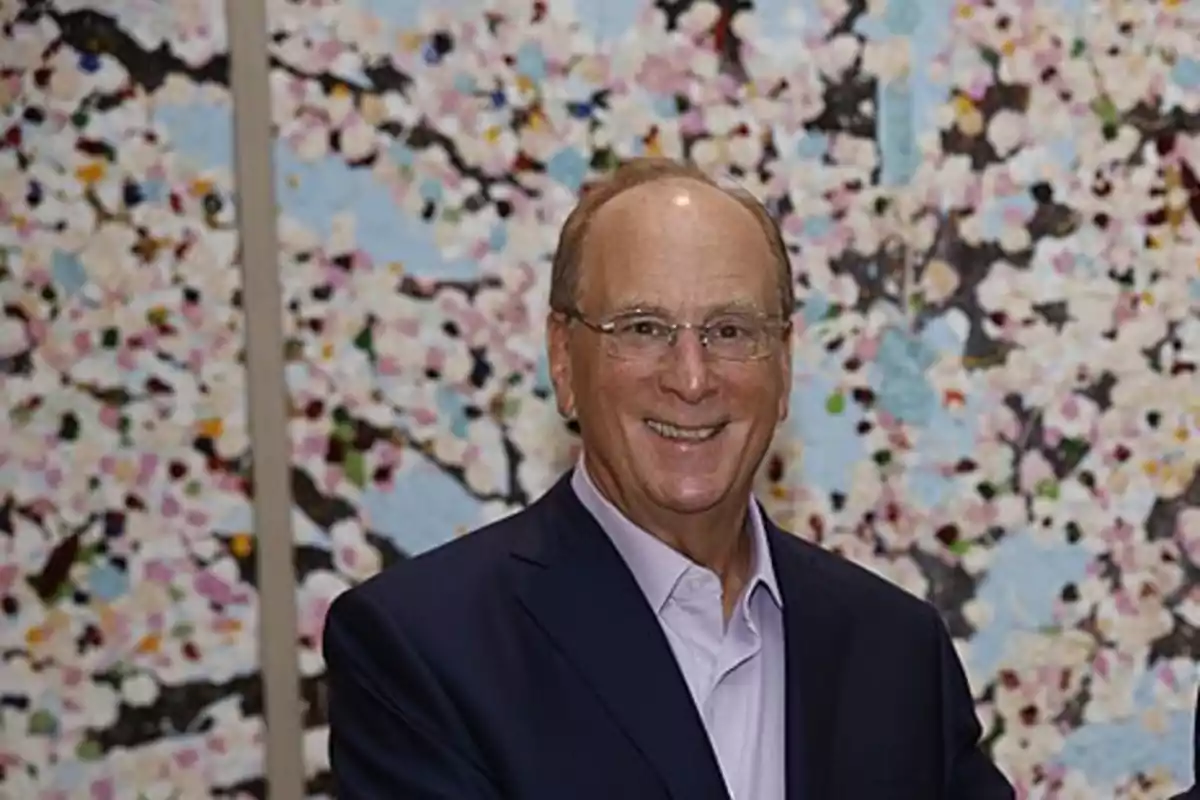 Hombre de mediana edad con gafas y traje oscuro sonriendo frente a un fondo colorido con motivos florales Hombre de mediana edad con gafas y traje oscuro sonriendo frente a un fondo colorido con motivos florales