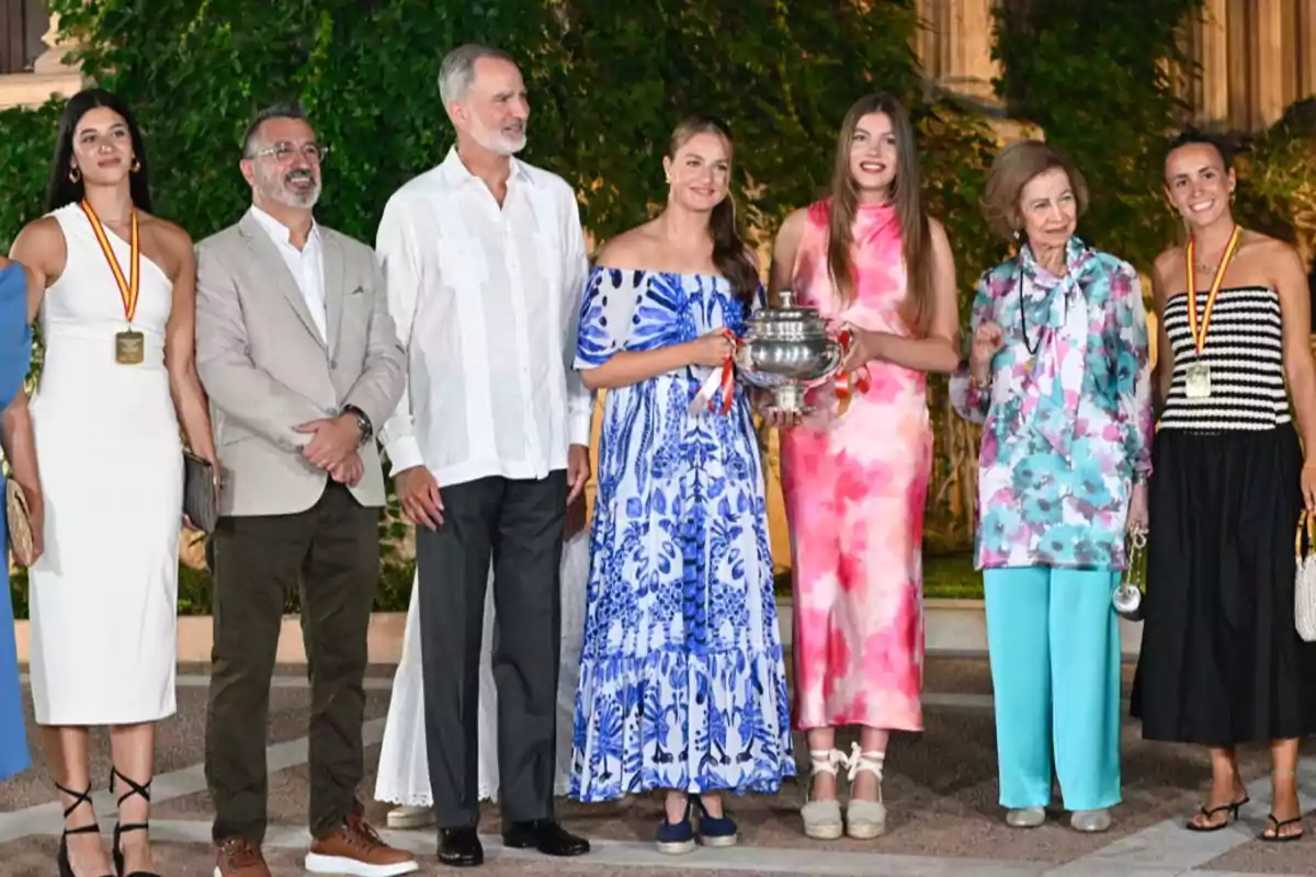 Grupo de personas posando al aire libre, algunas con medallas y una mujer sosteniendo un trofeo plateado