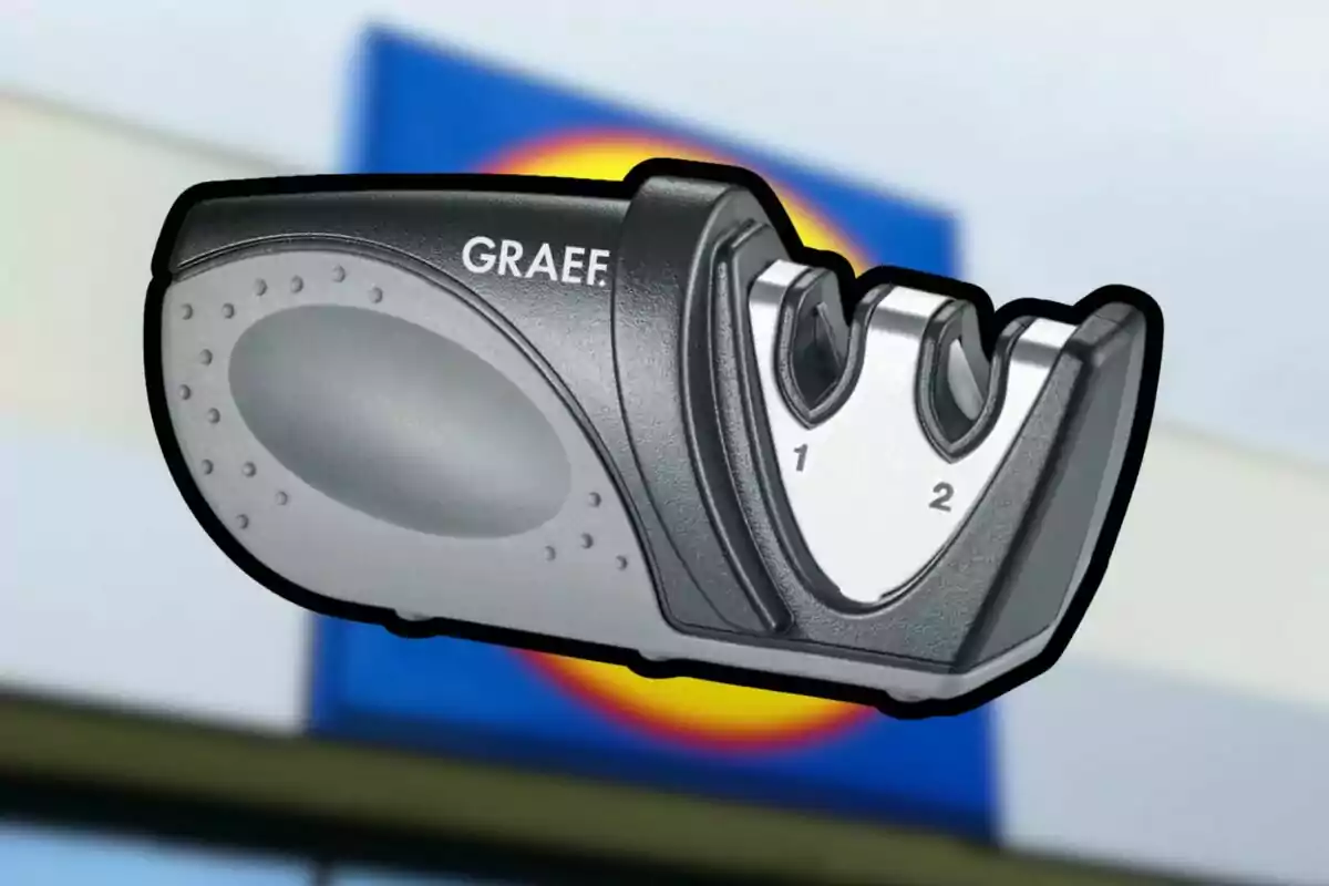 Afilador de cuchillos manual de la marca Graef con dos ranuras numeradas, sobre un fondo desenfocado de un letrero de supermercado. Afilador de cuchillos manual de la marca Graef con dos ranuras numeradas, sobre un fondo desenfocado de un letrero de supermercado.