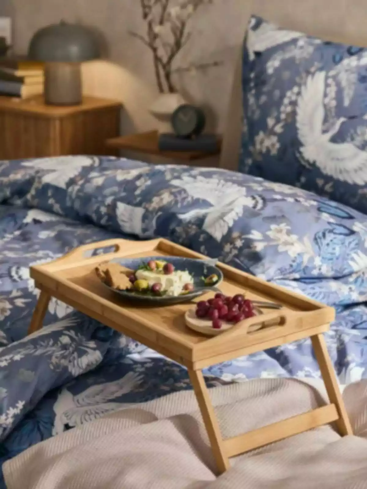 Desayuno servido en una bandeja de madera sobre una cama con ropa de cama azul decorada con grullas blancas Desayuno servido en una bandeja de madera sobre una cama con ropa de cama azul decorada con grullas blancas