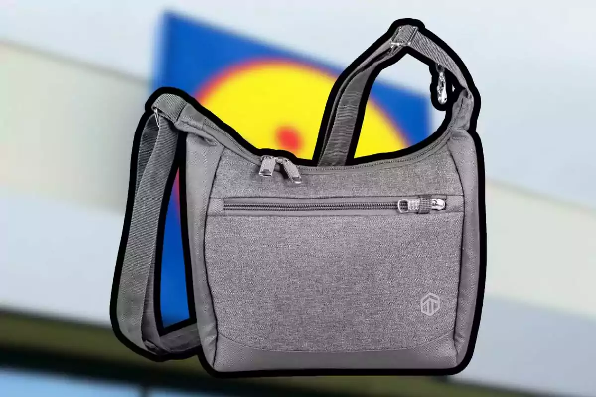 Bolso gris con cierre y correa ajustable sobre un fondo desenfocado con colores azul y amarillo Bolso gris con cierre y correa ajustable sobre un fondo desenfocado con colores azul y amarillo