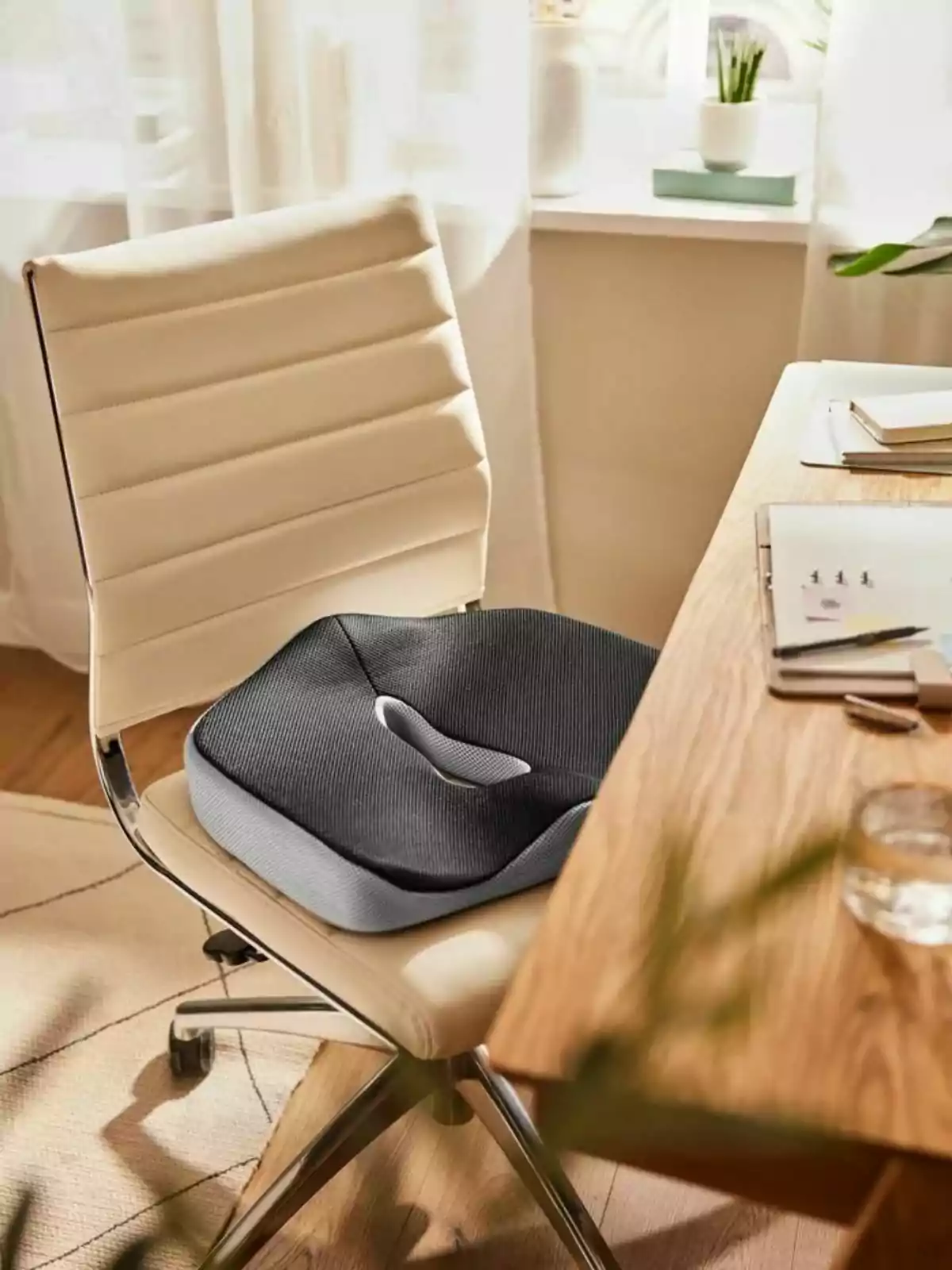 Cojín ergonómico negro sobre una silla de oficina blanca junto a un escritorio de madera en un ambiente iluminado y moderno Cojín ergonómico negro sobre una silla de oficina blanca junto a un escritorio de madera en un ambiente iluminado y moderno