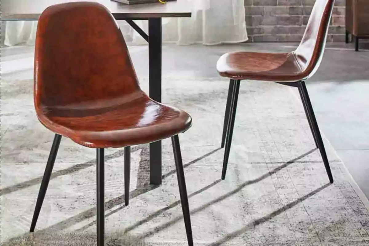 Dos sillas de diseño moderno con asiento marrón y patas negras sobre una alfombra clara en un comedor iluminado Dos sillas de diseño moderno con asiento marrón y patas negras sobre una alfombra clara en un comedor iluminado