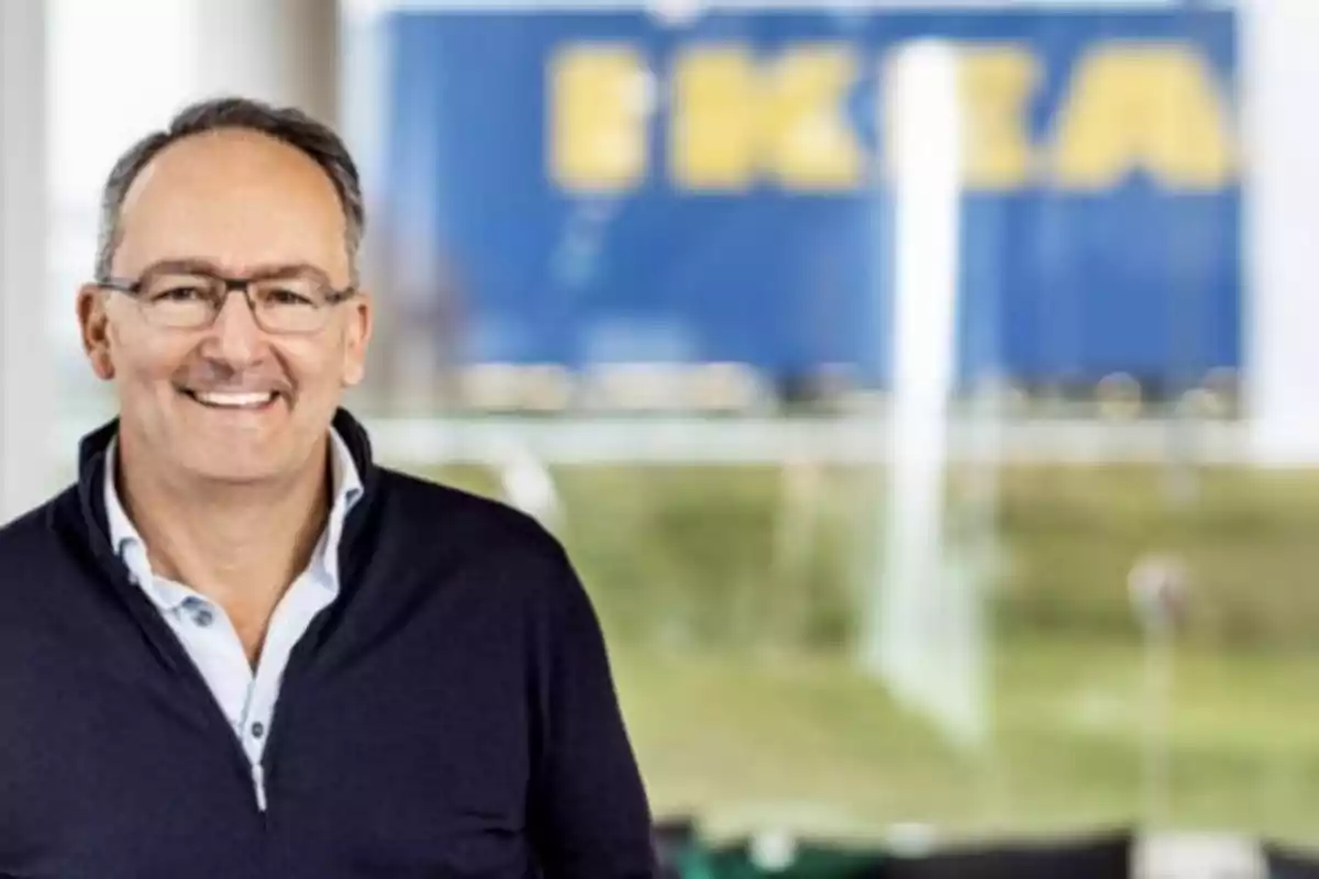 Hombre de mediana edad con gafas y suéter oscuro sonriendo frente a un fondo borroso con el logo de IKEA