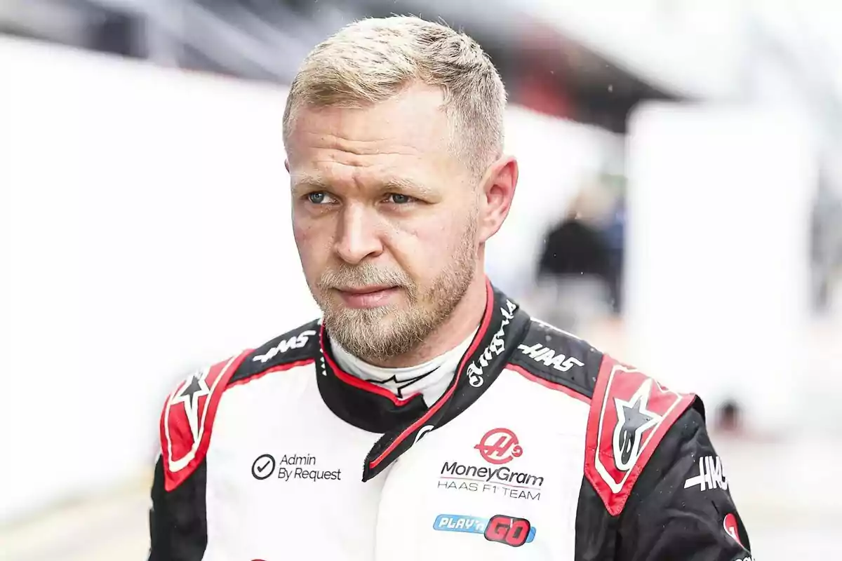 Piloto de automovilismo con traje de carreras blanco y negro del equipo Haas en un entorno de paddock Piloto de automovilismo con traje de carreras blanco y negro del equipo Haas en un entorno de paddock