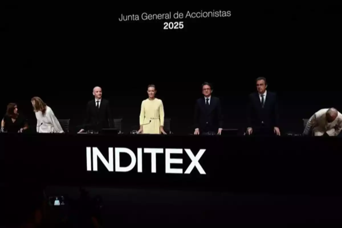Varios directivos de Inditex de pie en una mesa durante la Junta General de Accionistas 2025 con el logo de la empresa en grande al frente Varios directivos de Inditex de pie en una mesa durante la Junta General de Accionistas 2025 con el logo de la empresa en grande al frente