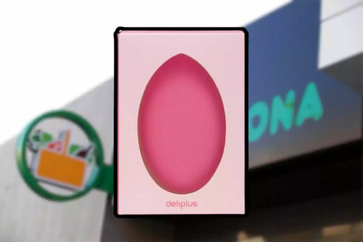 Esponja de maquillaje rosa de la marca Deliplus en su empaque frente a una tienda Mercadona desenfocada. Esponja de maquillaje rosa de la marca Deliplus en su empaque frente a una tienda Mercadona desenfocada.