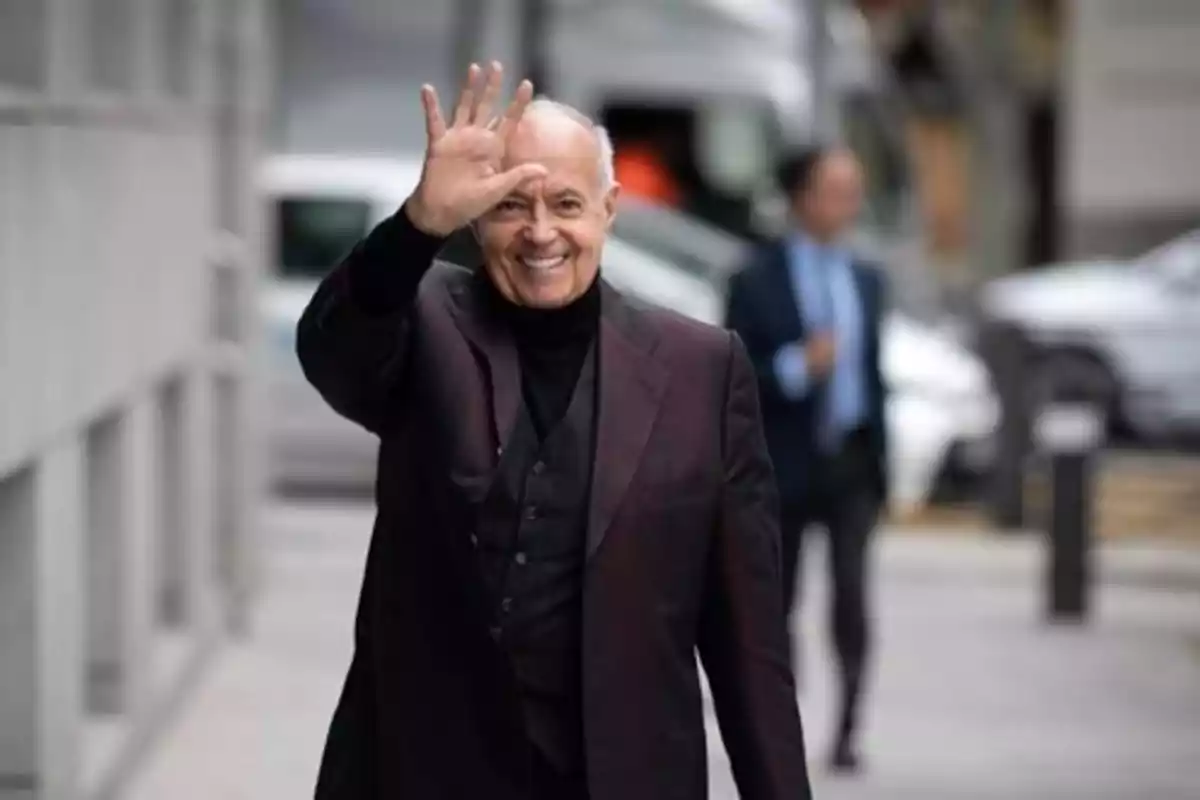 Hombre mayor sonriente saludando con la mano mientras camina por la calle vestido con traje oscuro Hombre mayor sonriente saludando con la mano mientras camina por la calle vestido con traje oscuro