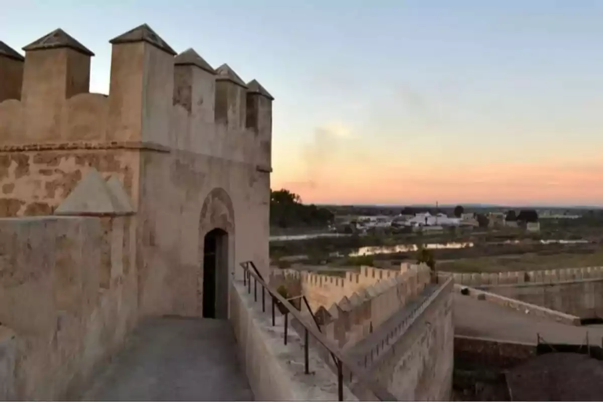 Murallas de una fortaleza antigua al atardecer con vista a un paisaje rural y algunas edificaciones al fondo Murallas de una fortaleza antigua al atardecer con vista a un paisaje rural y algunas edificaciones al fondo