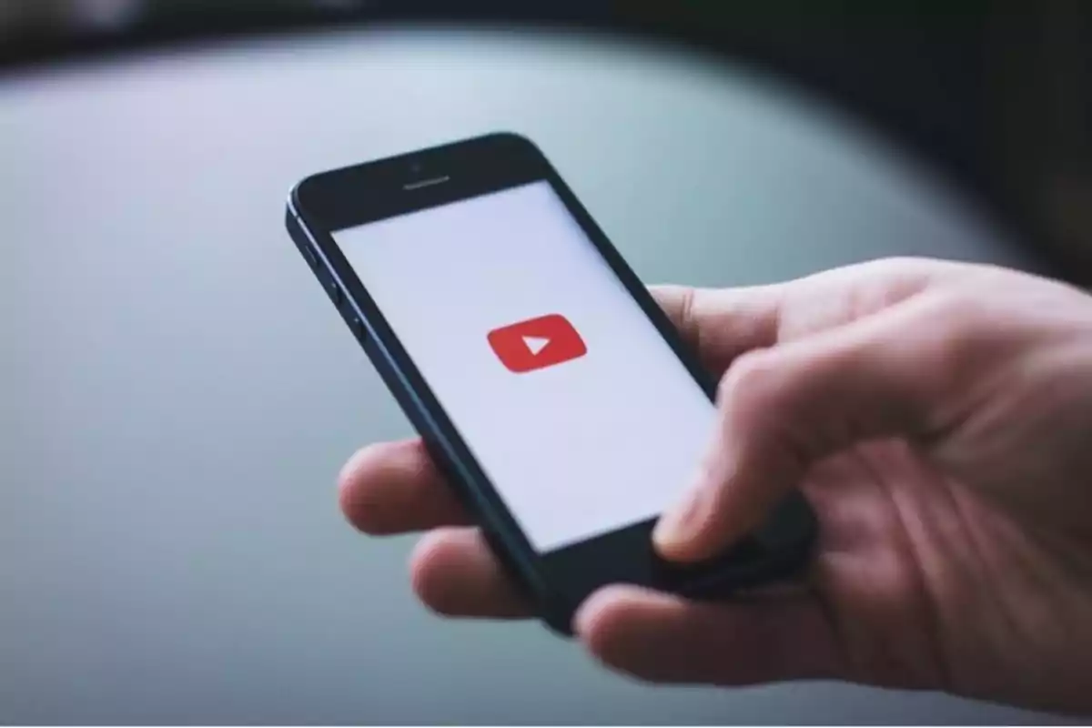 Persona sosteniendo un teléfono móvil que muestra el logo de YouTube en la pantalla Persona sosteniendo un teléfono móvil que muestra el logo de YouTube en la pantalla