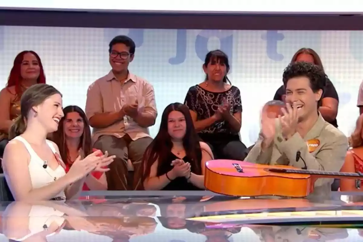Isabel Moreno y Alfred Garcia sonríen y aplauden en un programa de televisión mientras una guitarra descansa sobre la mesa y el público los observa y también aplaude. Captura de 'Pasapalabra' Isabel Moreno y Alfred Garcia sonríen y aplauden en un programa de televisión mientras una guitarra descansa sobre la mesa y el público los observa y también aplaude. Captura de 'Pasapalabra'