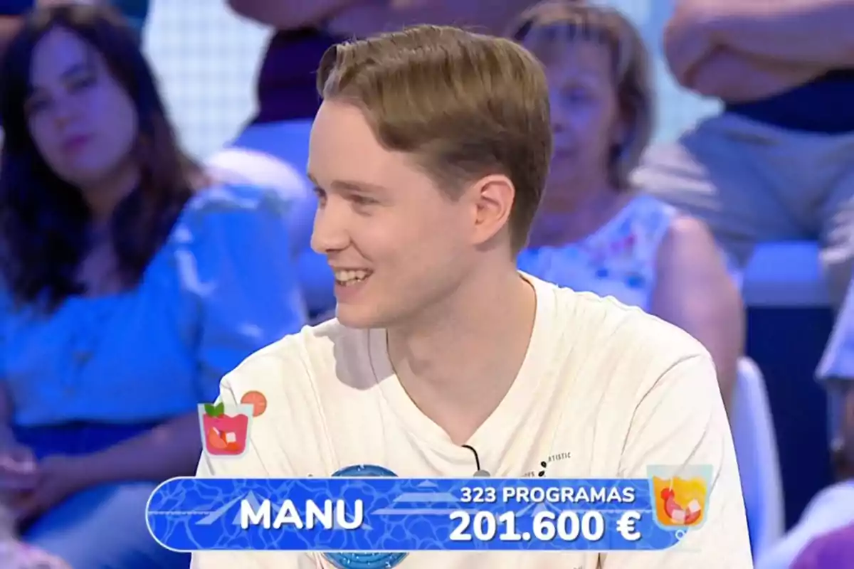 Manu sonriente participa en un concurso de televisión, lleva una camiseta blanca y en la pantalla aparece su nombre, el número de programas en los que ha participado y la cantidad de dinero acumulada. Captura de 'Pasapalabra' Manu sonriente participa en un concurso de televisión, lleva una camiseta blanca y en la pantalla aparece su nombre, el número de programas en los que ha participado y la cantidad de dinero acumulada. Captura de 'Pasapalabra'