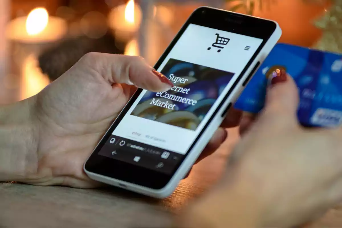 Persona usando un teléfono móvil para hacer compras en línea mientras sostiene una tarjeta de crédito
