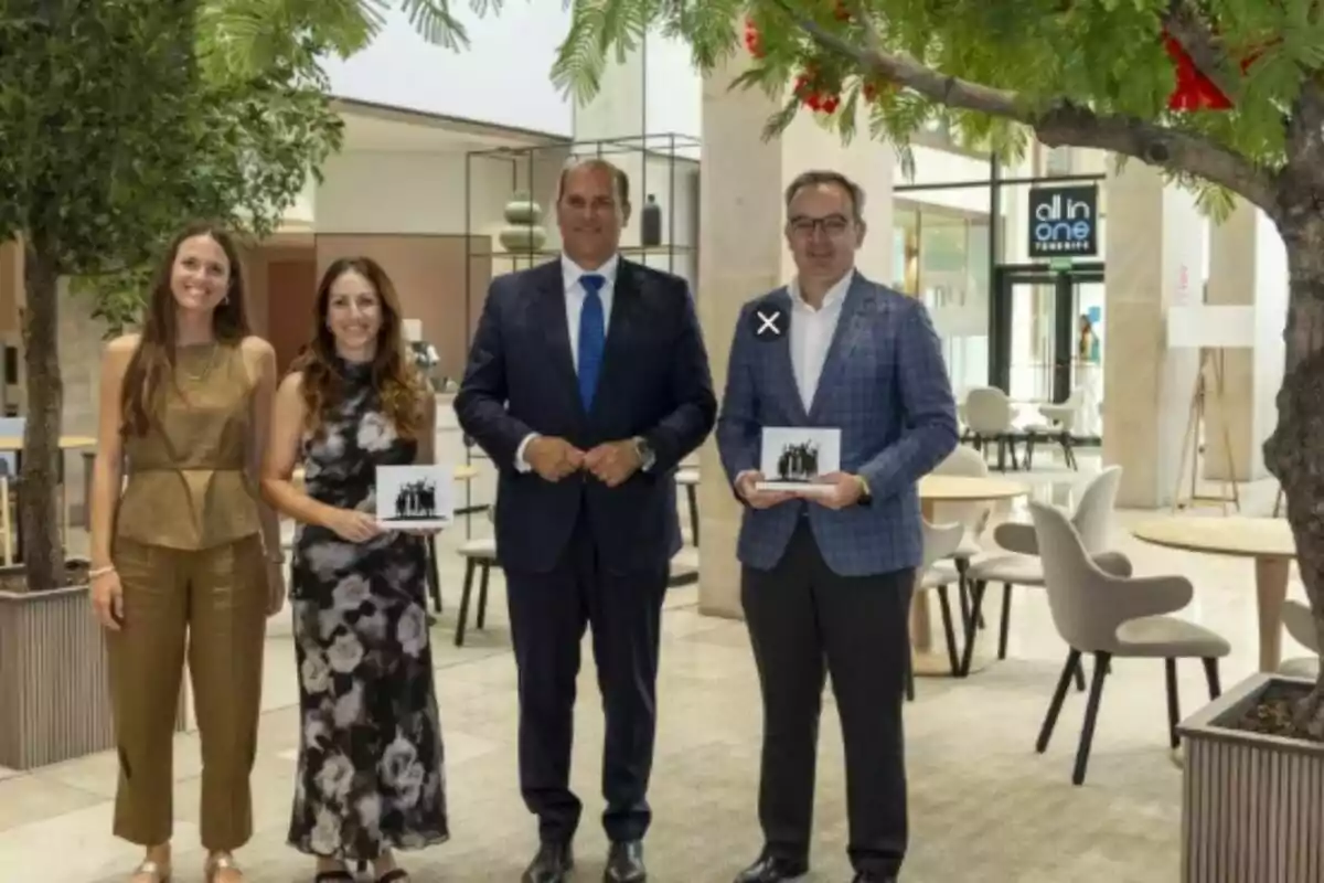 Cuatro personas posan sonrientes en un espacio interior moderno con árboles y mesas, dos de ellas sostienen un reconocimiento en las manos.